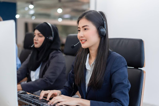 Two professional female virtual assistants wearing headsets work at computers in a modern office, representing businesses that choose to outsource their operations for increased efficiency.