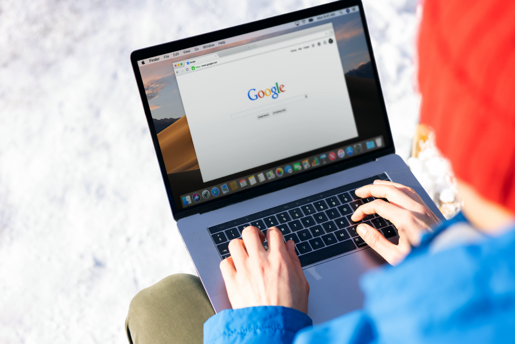 Person in a red beanie and blue jacket using a laptop outdoors in a snowy setting, with the Google homepage open on the screen—symbolizing the importance of online visibility and SEO for business success.