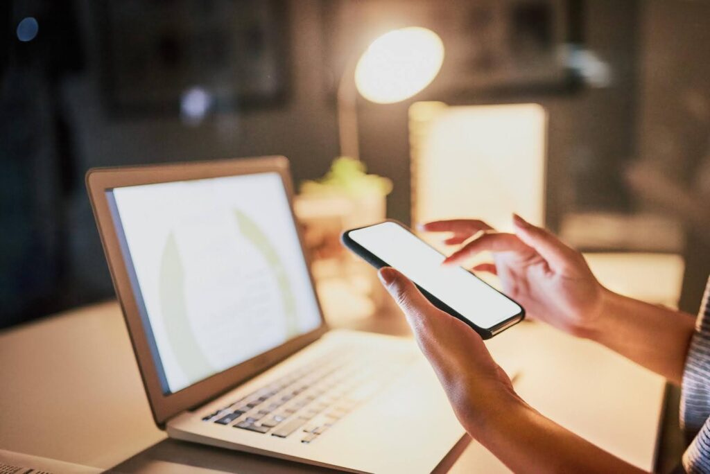 Person using a smartphone and laptop at a desk under warm lighting, emphasizing that posting alone isn’t a content strategy.