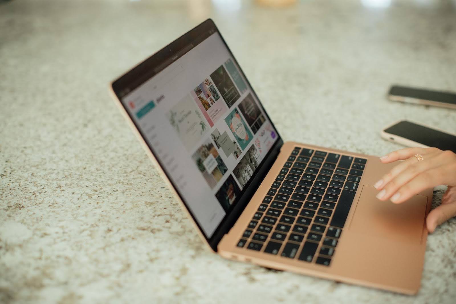 Person using Canva on a rose gold laptop to browse templates, highlighting the risks of using generic Canva templates for branding.