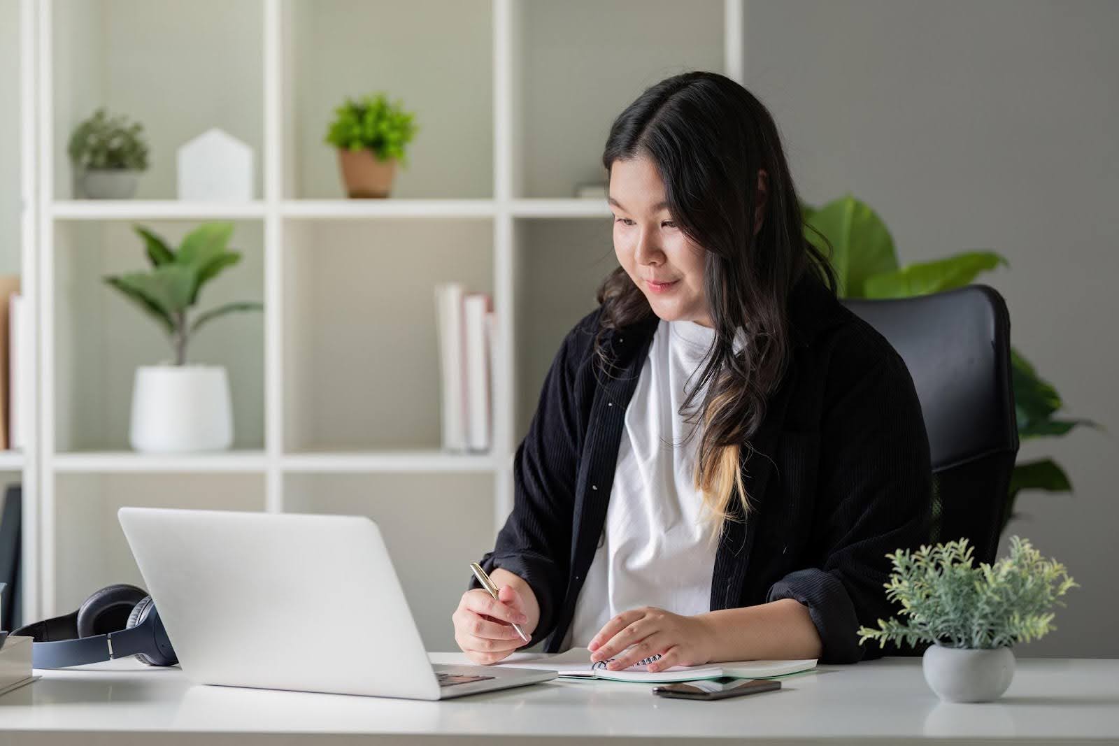Woman working at a desk with a laptop and taking notes, representing tasks that can be offloaded to a virtual assistant.