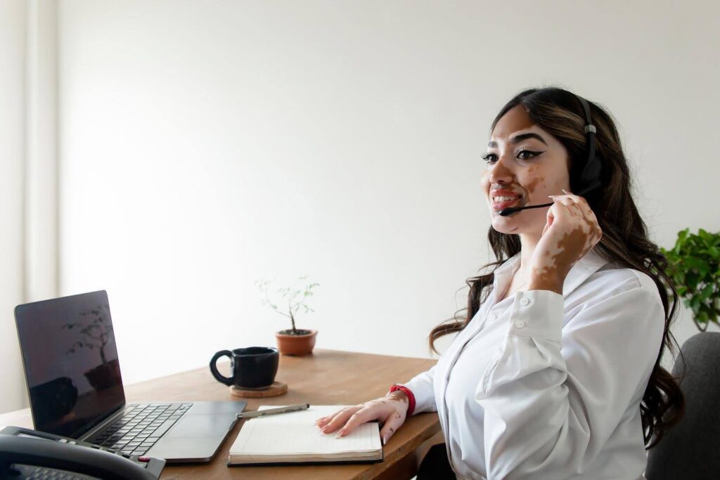 Smiling woman with a headset working at a desk with a laptop, notebook, and coffee mug—representing BPO (Business Process Outsourcing) support for front-line and back-office efficiency.