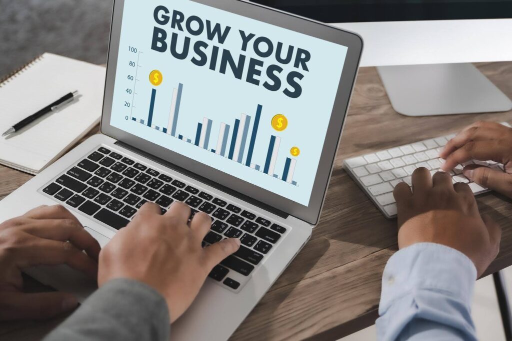 Hands typing on laptop showing chart with 'Grow Your Business' text, representing strategies to grow a Facebook page organically in 2025.