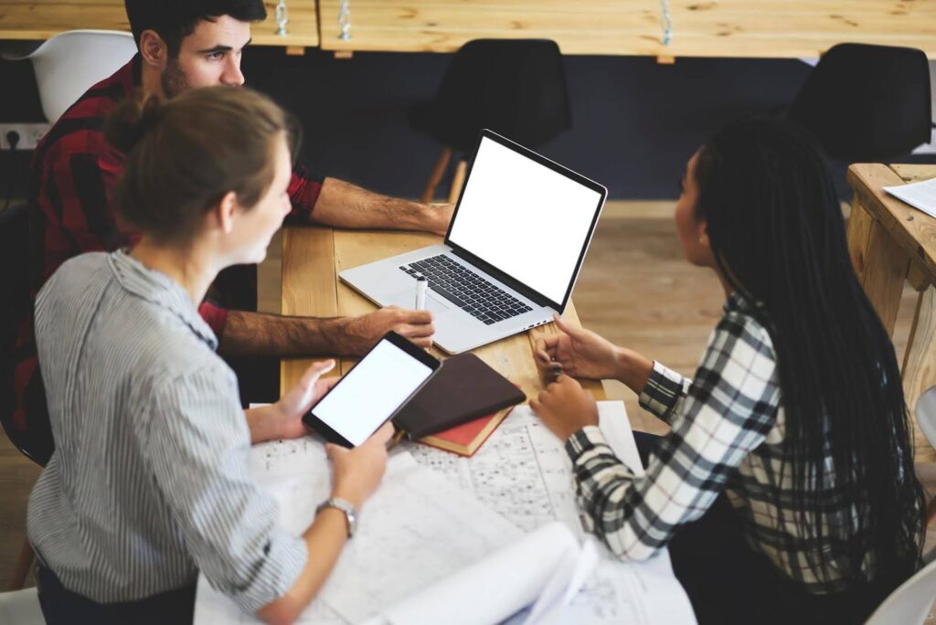 Group of young professionals collaborating with laptops and tablets, discussing strategies to avoid a business mistake in franchising.