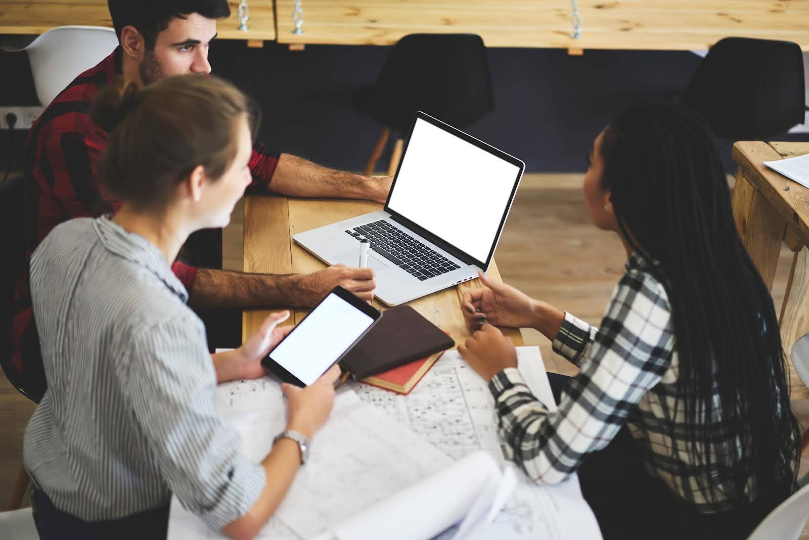 Group of young professionals collaborating with laptops and tablets, discussing strategies to avoid a business mistake in franchising.