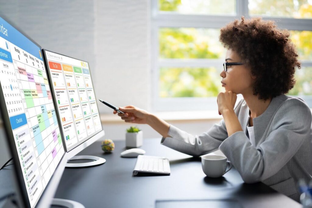 Focused professional reviewing tasks and schedules on dual monitors, representing the role of a project manager in organizing and overseeing workflows