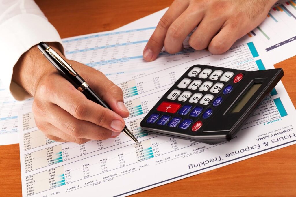 Close-up of a person using a calculator and reviewing financial documents, symbolizing the importance for startups to track expenses accurately for taxes.