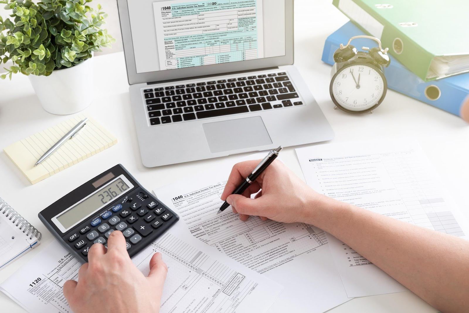Person using a calculator and filling out tax forms at a desk with a laptop, symbolizing how poor bookkeeping can harm a professional’s credibility.