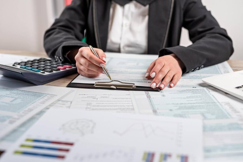 Business professional reviewing financial documents and forms with a calculator and charts on the desk, representing quarterly tax planning and financial preparation for small businesses under $100K.