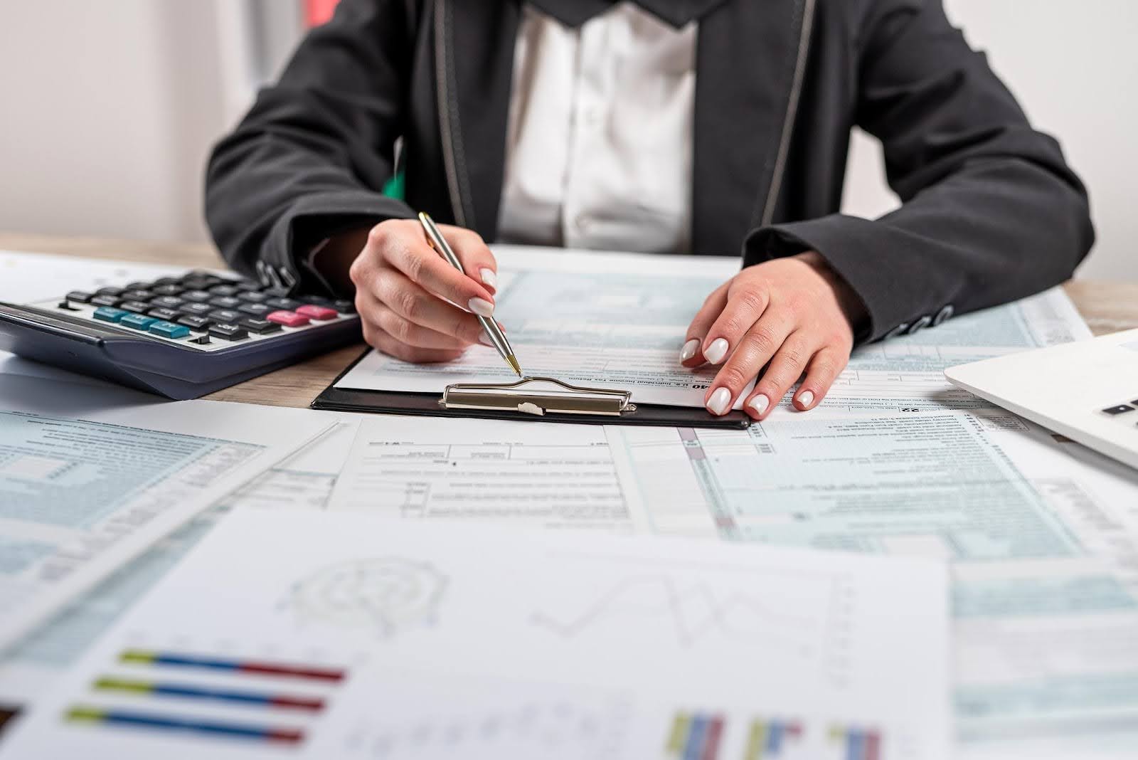 Business professional reviewing financial documents and forms with a calculator and charts on the desk, representing quarterly tax planning and financial preparation for small businesses under $100K.