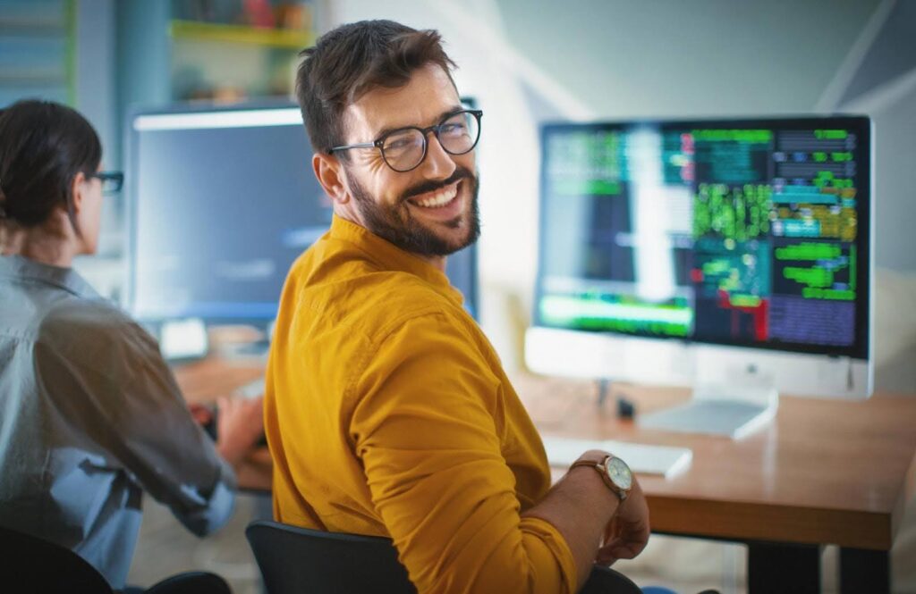 Smiling man in glasses working on code at a computer, representing web development services tailored for founders who want effective websites without dealing with technical complexity.