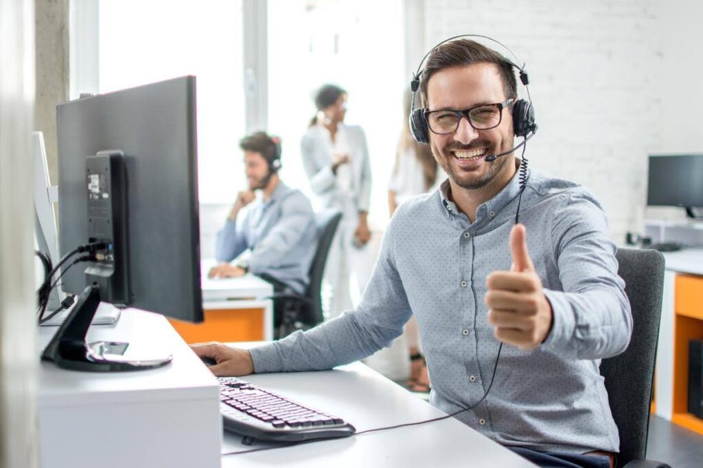 Customer service representative wearing a headset and giving a thumbs-up at his desk, highlighting the importance of maintaining customer service quality as a business grows.