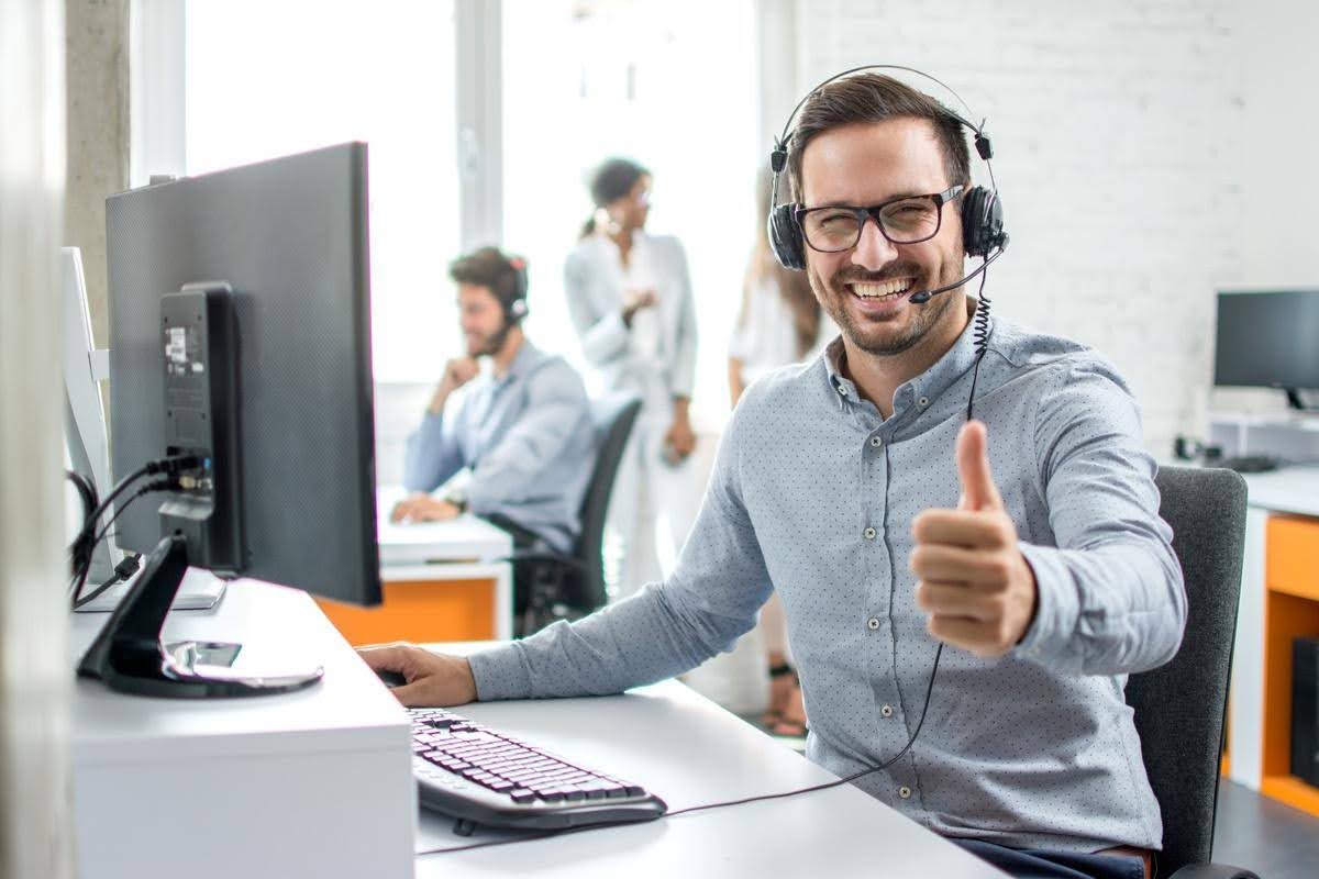 Customer service representative wearing a headset and giving a thumbs-up at his desk, highlighting the importance of maintaining customer service quality as a business grows.